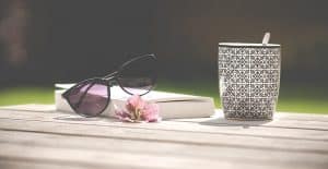 Een tafel met zonnebril, bloem, boek en een mok
